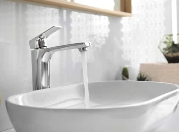 Running faucet pouring water into a small white basin kitchen sink