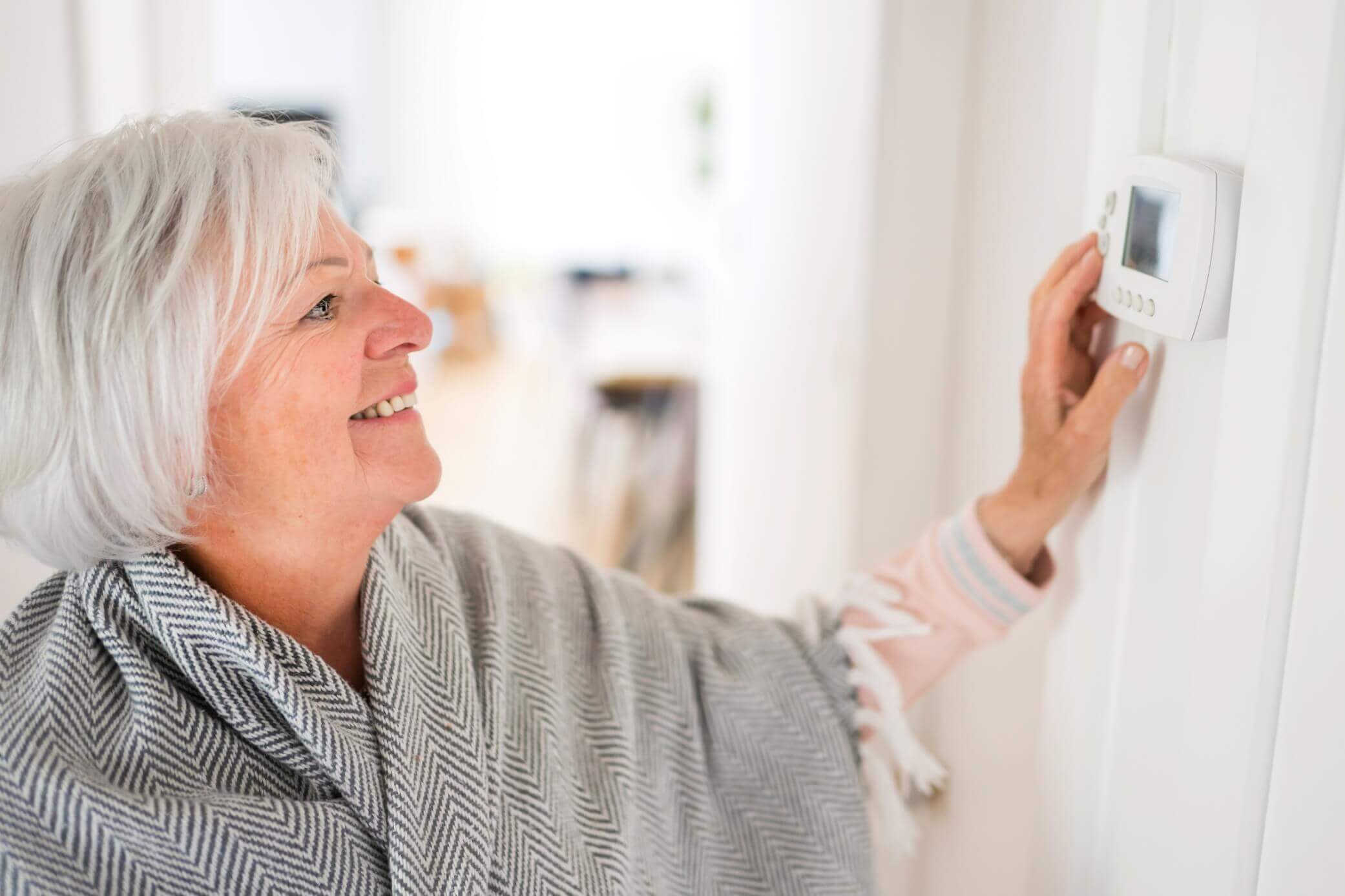 Older woman set the thermostat on wall