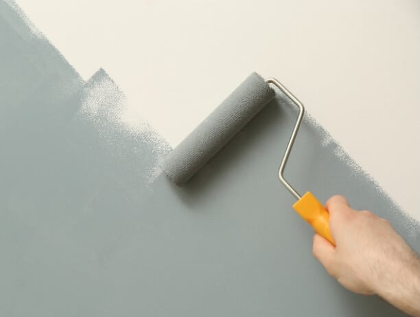 Man painting green greyish paint on top of beige wall